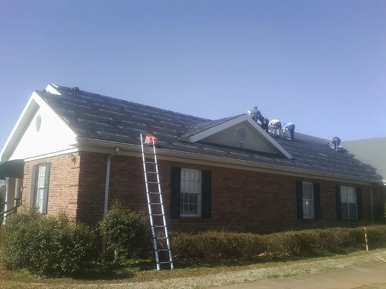 Crew tearing shingles off a brick ranch roof with a ladder set — Emergency Roof Repair work by our crew in North Adams