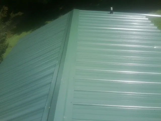 New green metal panels meeting at the ridge of a roof — Flat Roof Repair work by our crew in North Adams