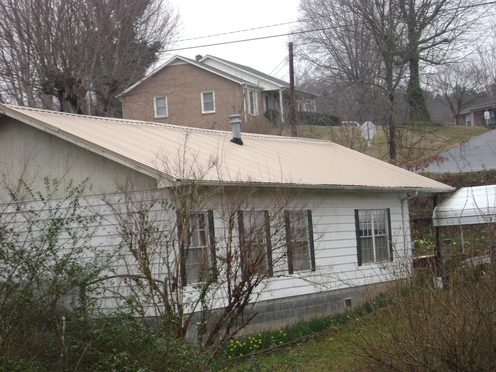 Tan metal roof on a white sided house set into a hillside — Commercial Roofing by Roofing Brothers in North Adams