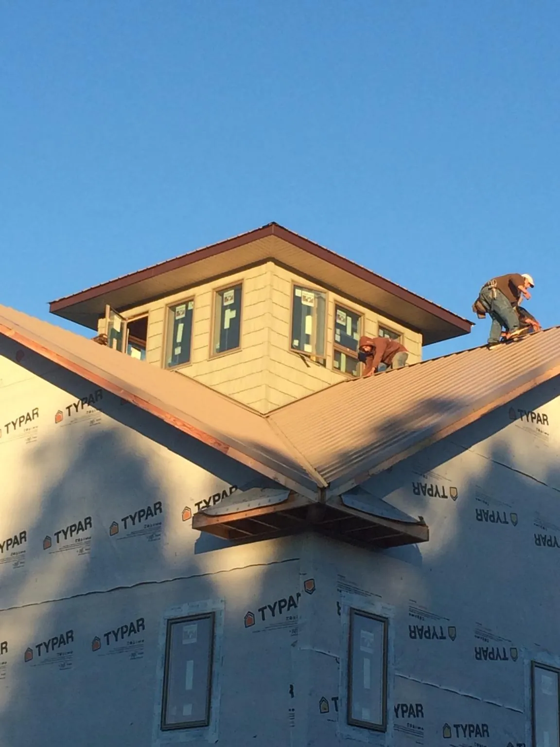 Roofers working around a rooftop cupola on a new metal roof at sunset in North Adams